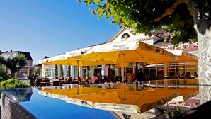 A hotel with outdoor seating under yellow umbrellas, a pool reflecting the building, and a clear blue sky. - Kurpark-Hotel Bad Dürkheim (Bad Durkheim)