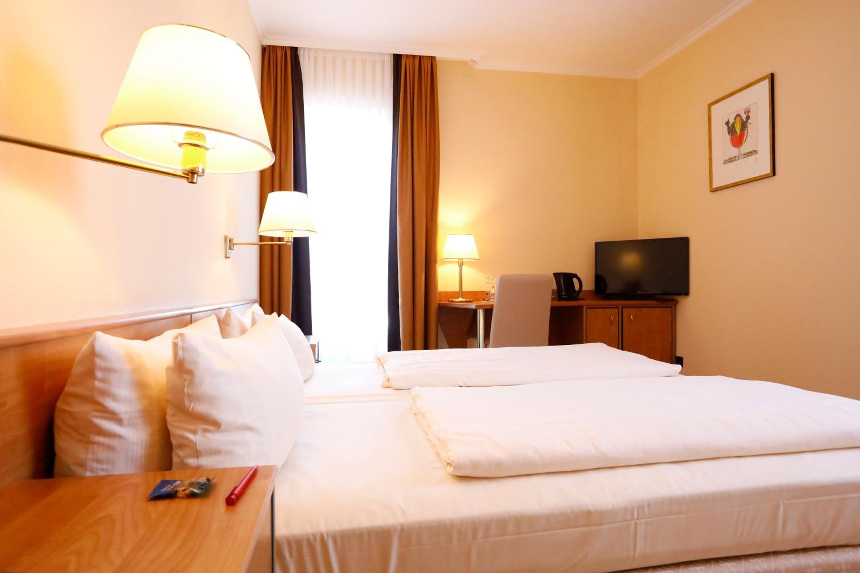 A hotel room with two beds, a desk with a lamp, a television, and a framed picture on the wall.