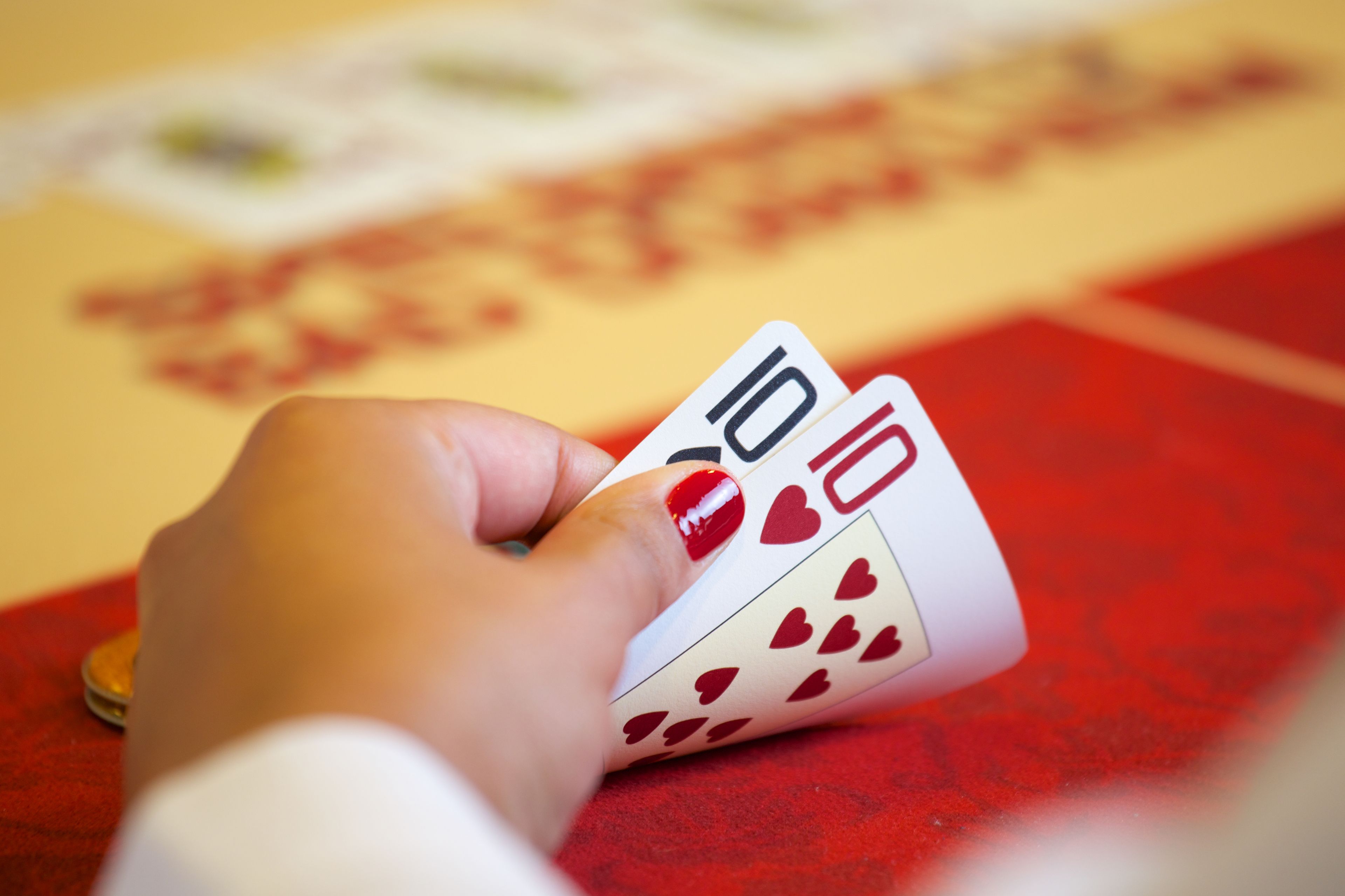 A hand holding playing cards with a red tablecloth in the background.