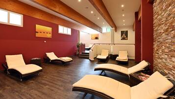 Un cuarto de spa con vigas de madera, paredes rojas y varios sillones de sol.