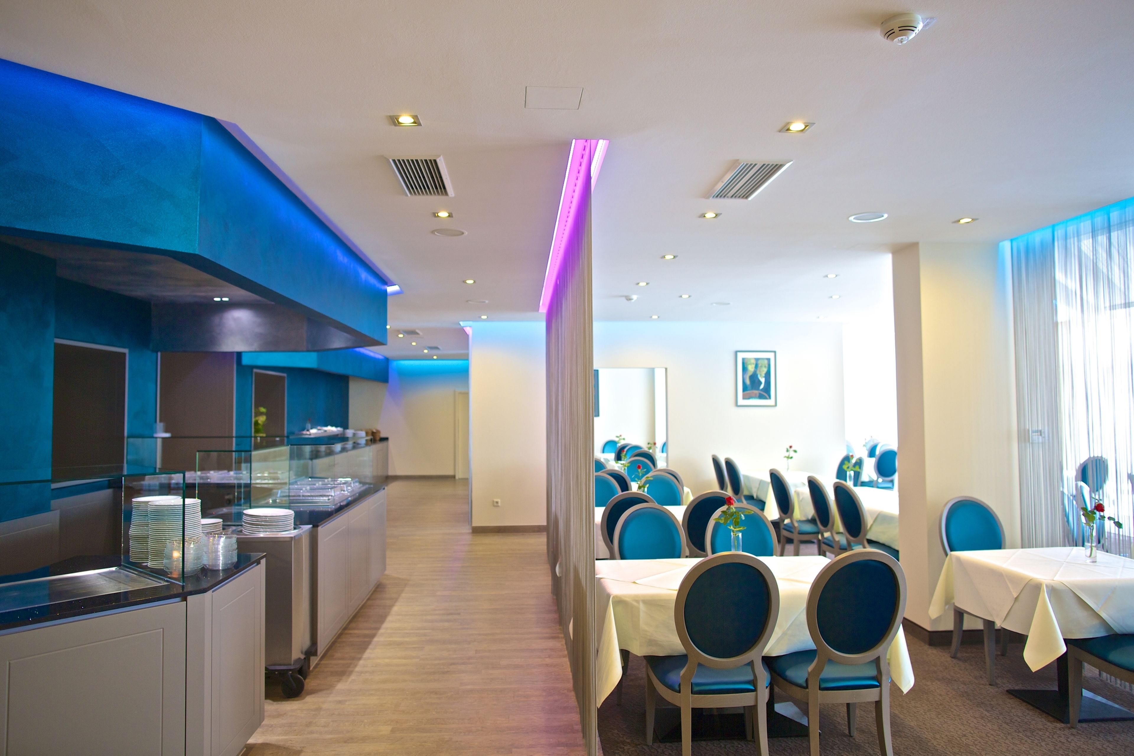 Ein Hotel-Speisesaal mit einem Buffet links, Tischen mit blauen Stühlen und Blick auf den Speisesaal im Hintergrund.