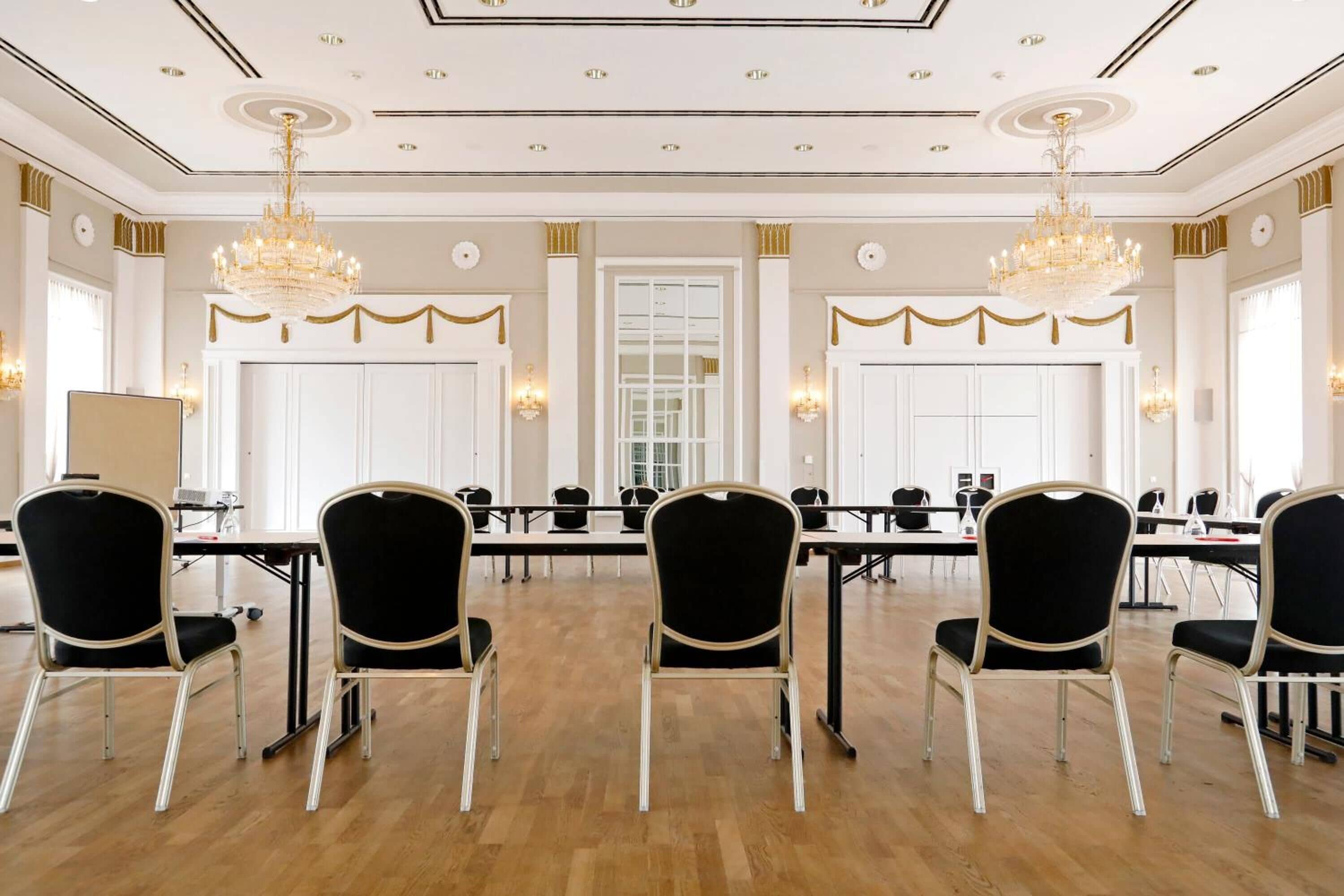 A conference room with a long table, black chairs, chandeliers, and white walls.