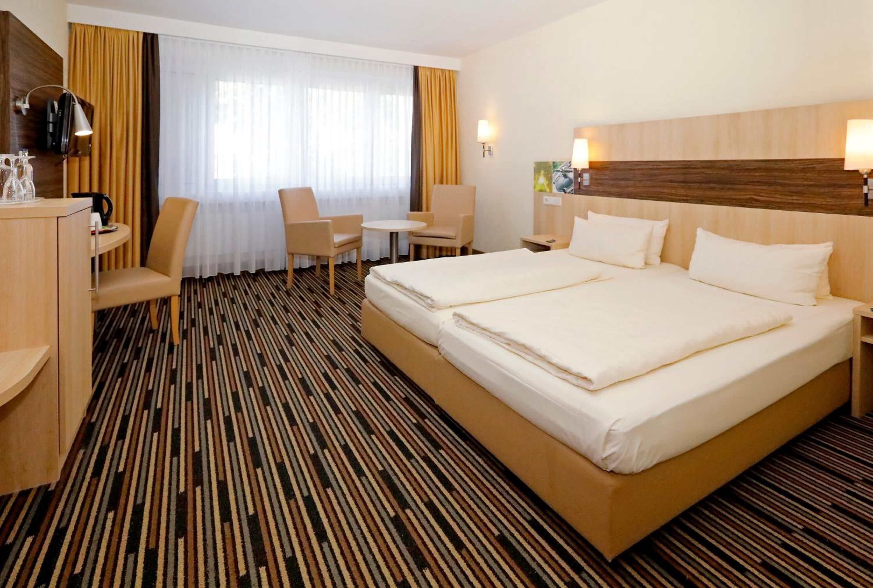 Ein Hotelzimmer mit einem großen Bett, zwei Stühlen, einem kleinen Tisch und einem Schreibtisch mit einer Lampe.