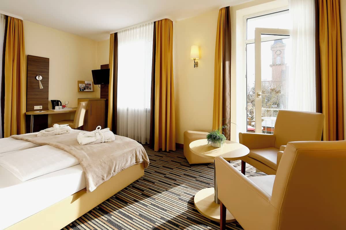 Une chambre d’hôtel avec un lit, un bureau, une chaise, une petite table et une vue sur un immeuble par la fenêtre.