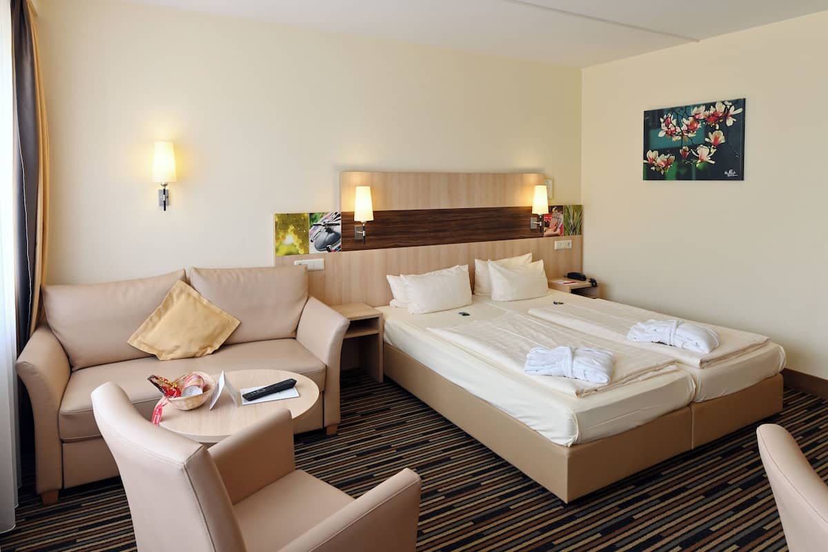 Une chambre d’hôtel avec un lit, un canapé, une petite table et un téléviseur fixé au mur.