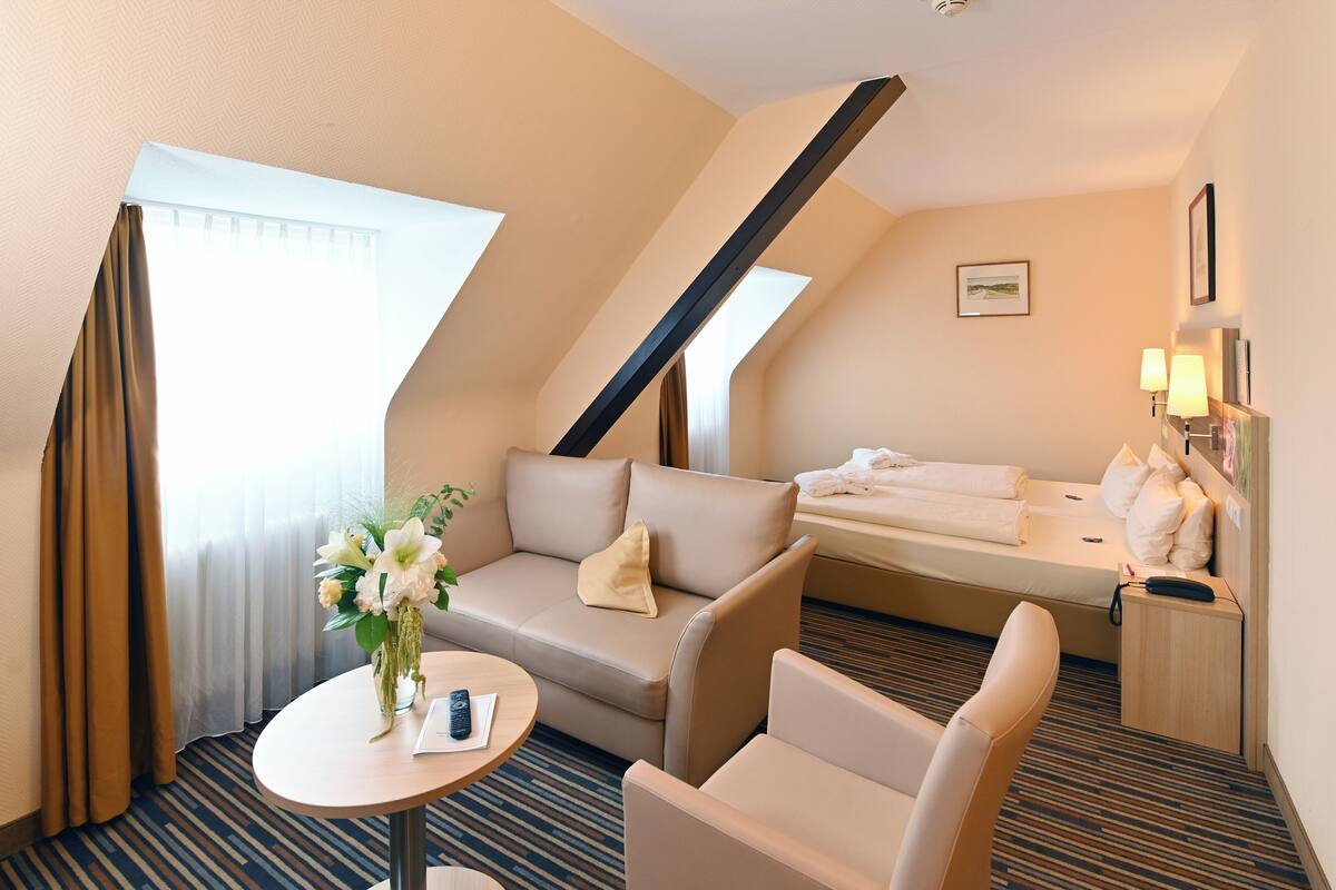 Une chambre d’hôtel avec un canapé, un lit, une petite table ornée d’un vase de fleurs et un bureau avec une lampe.