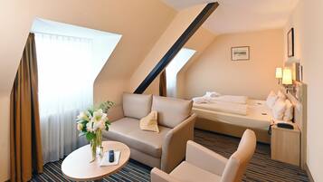Ein Hotelzimmer mit einer Couch, einem Bett, einem kleinen Tisch mit Blumenvase und einem Schreibtisch mit Lampe.