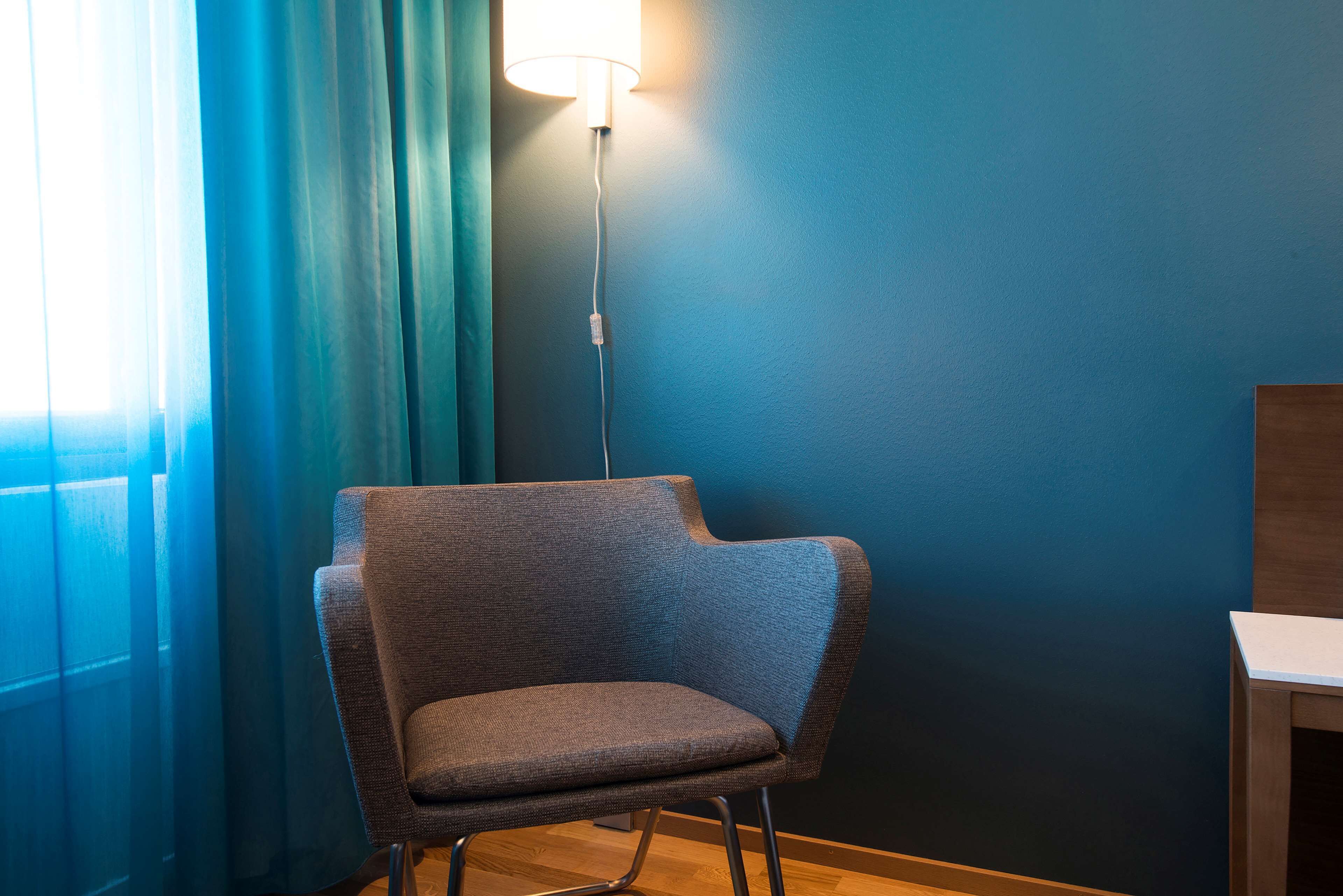 Ein Stuhl mit einer Lampe darüber, ein Fenster mit Vorhängen und eine blaue Wand.