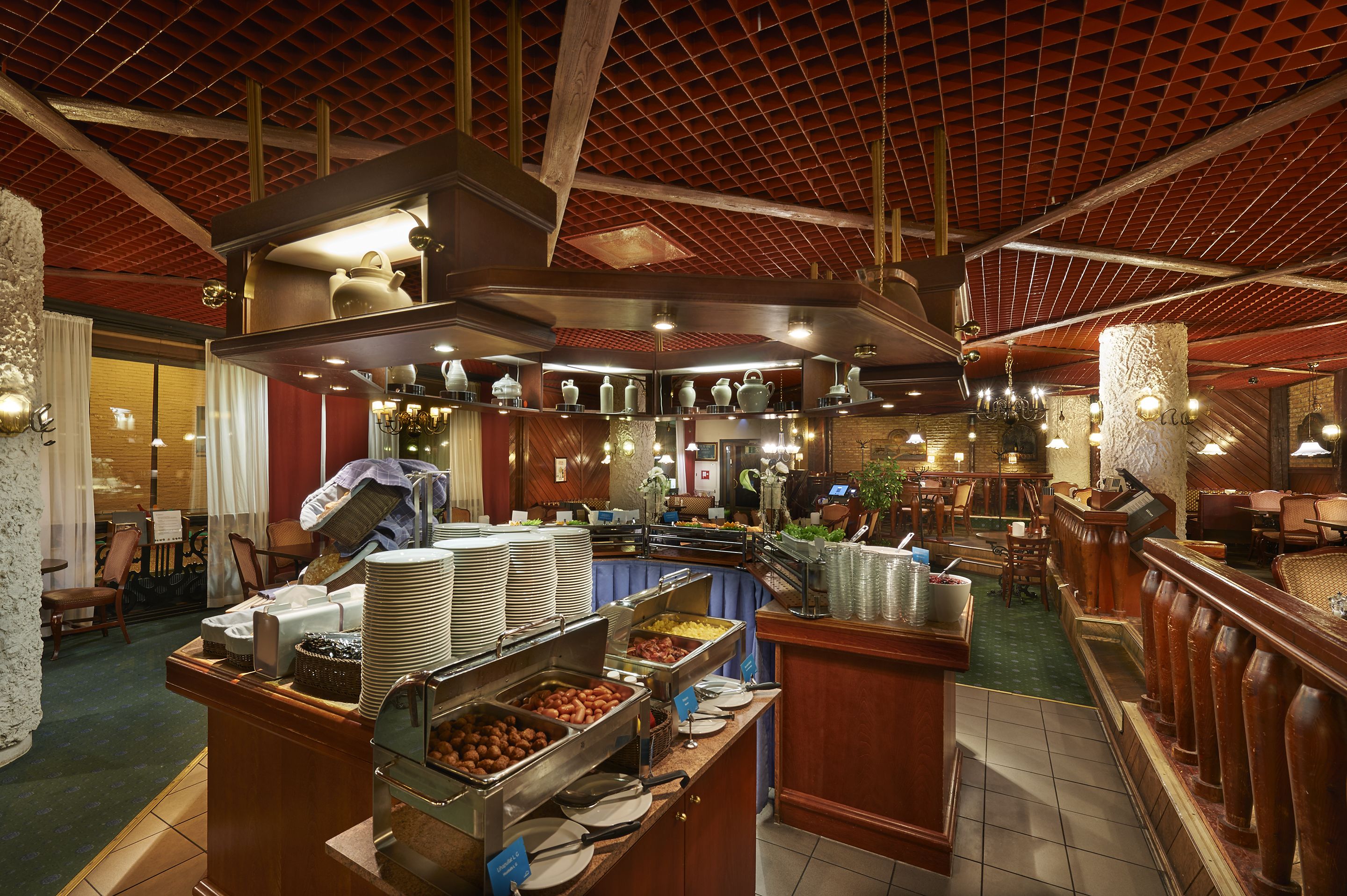 Een buffetgedeelte met diverse stations, een zithoek met tafels en stoelen, en een hoge ruimte met zichtbare balken.