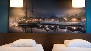 Une chambre d’hôtel avec une grande fresque murale représentant un paysage de bord de mer, deux lits avec du linge de maison blanc et une tête de lit en bois.