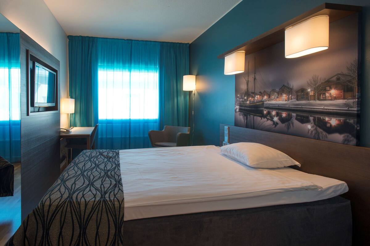 Una habitación de hotel con una cama, un escritorio, una silla y un cuadro en la pared.