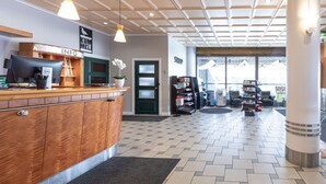 Un espace d’accueil avec un comptoir en bois, une enseigne « INFO », une enseigne « MAGASIN » et une vue sur l’extérieur grâce à de grandes fenêtres.