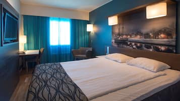 A hotel room with a large bed, a desk with a chair, a TV, and a painting on the wall.