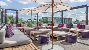 Un área de lounge en la azotea con asientos al aire libre, sombrillas y vistas de la ciudad.