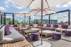 Eine Dachterrasse mit Sitzgelegenheiten im Freien, Sonnenschirmen und Blick auf die Stadt.