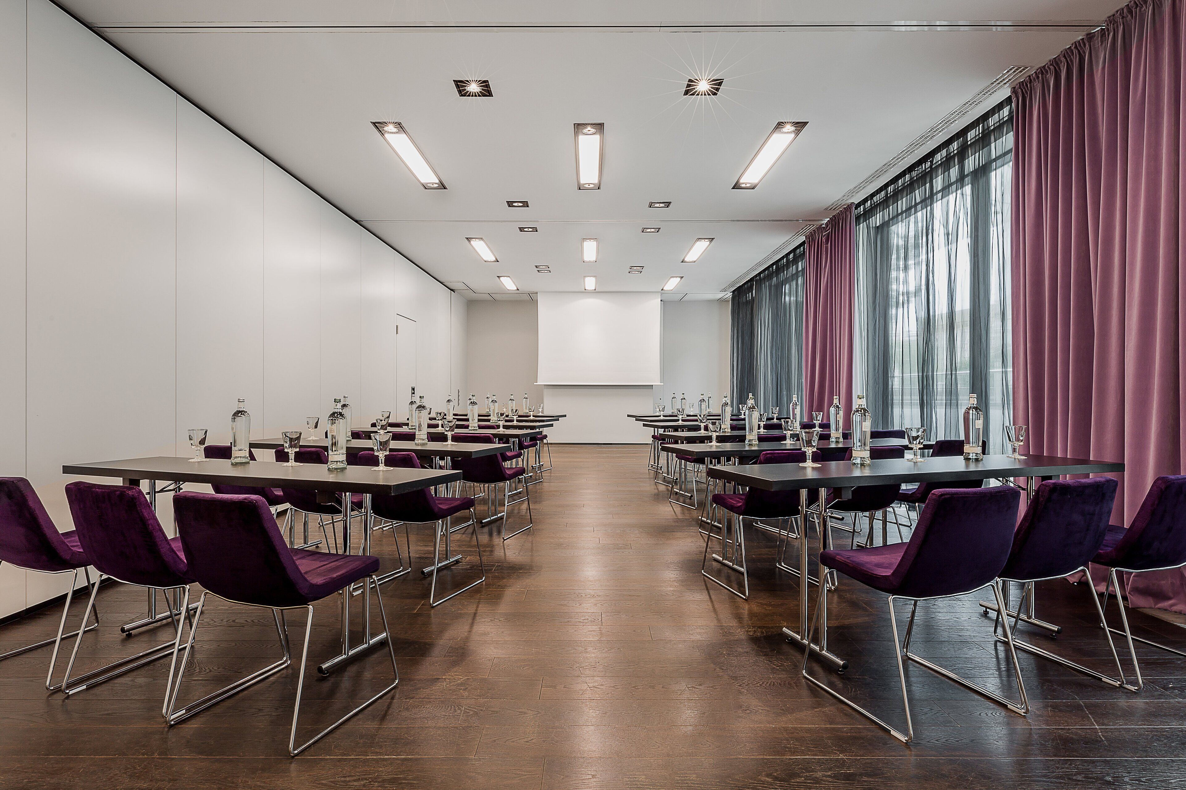 A conference room with a long table, chairs, and a projector screen.