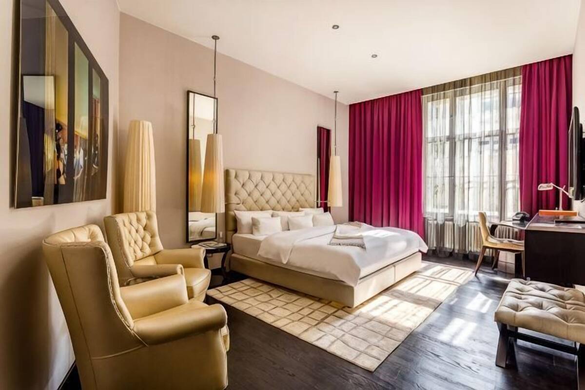 A hotel room with a large bed, a desk, a chair, a sofa, and a TV.