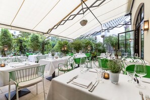 An outdoor dining area with tables set for two, surrounded by green chairs and white tablecloths. - Hotel Zoo Berlin (Berlin)