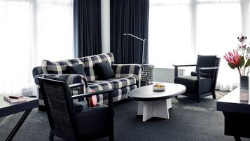 Un salon moderne avec un canapé à carreaux, des fauteuils noirs, une table basse ronde et une table d’appoint sur laquelle se trouvent un livre et un sac à main.