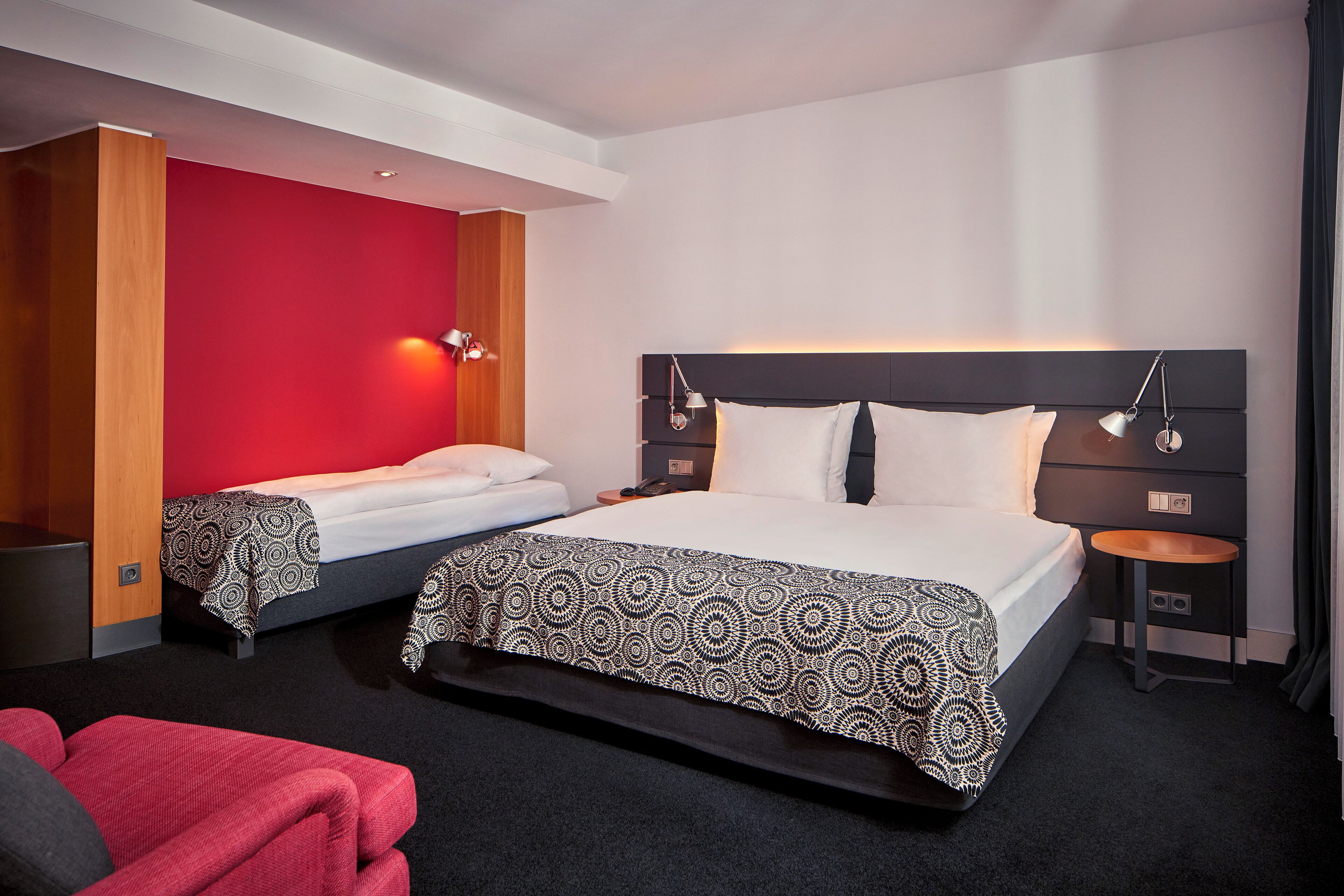 Habitación de hotel con una cama grande, una cama más pequeña, una pared de acento roja y una silla roja.
