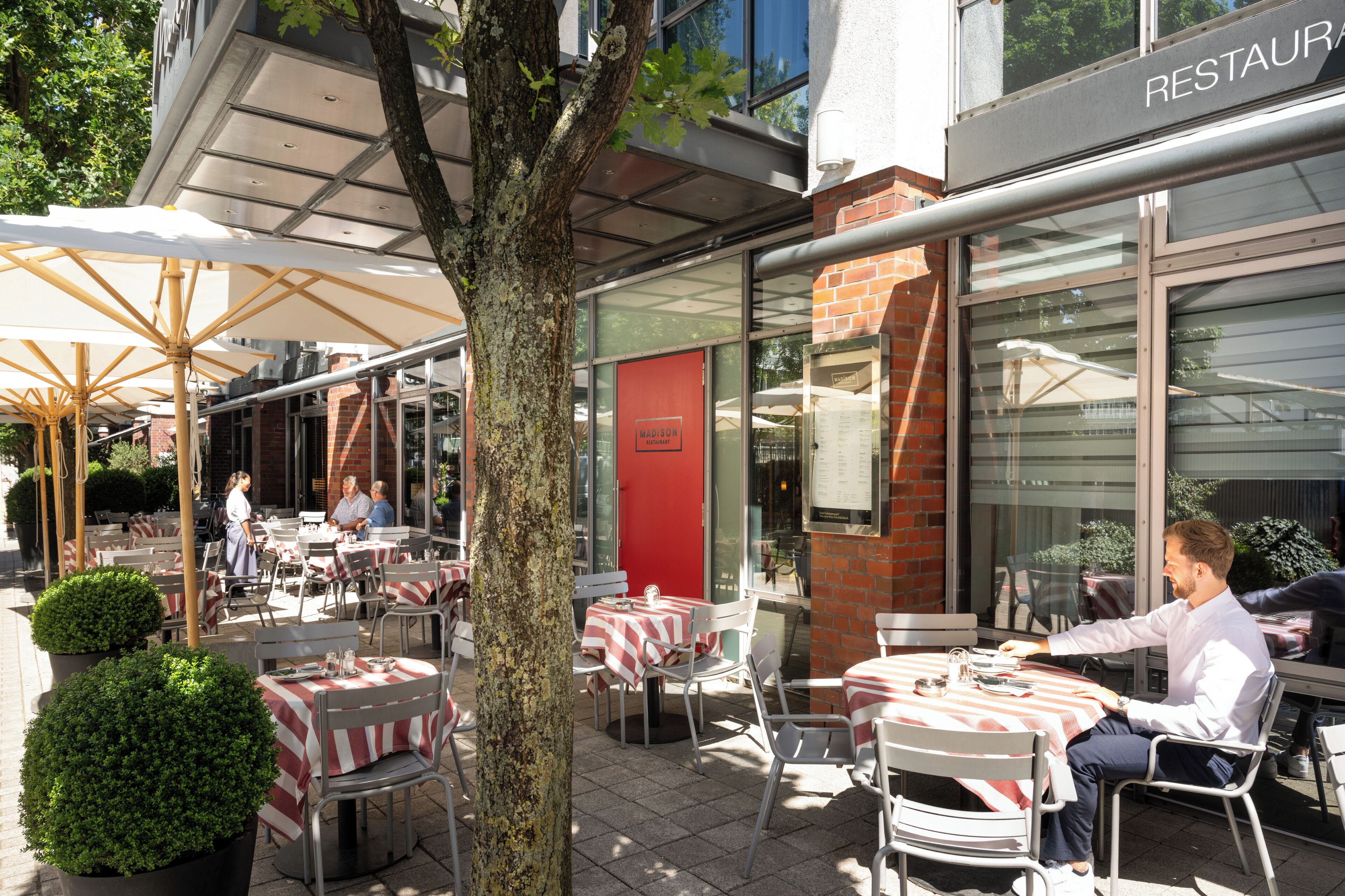 An outdoor dining area with tables and chairs, a tree, and a building with a 'RESTAURANT' sign.