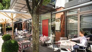 An outdoor dining area with tables and chairs, a tree, and a building with a 'RESTAURANT' sign.