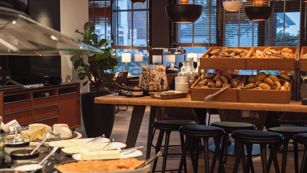 Zona de bufé con diversos alimentos, una planta grande y lámparas colgantes.