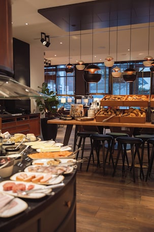 A buffet area with various food items, a large plant, and hanging pendant lights.. THE MADISON Hotel Hamburg