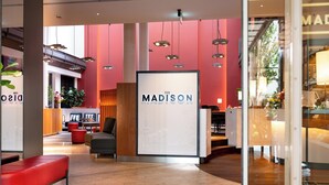 Un vestíbulo moderno con un cartel grande que dice 'The Madison', paredes rojas y zonas de estar.