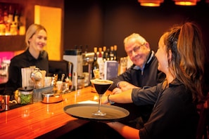 A bar setting with a martini glass on a tray, a bartender, and a customer.