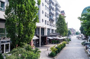 A building with a sign 'The Madison' on the ground floor, surrounded by trees and a cobblestone street. - THE MADISON Hotel Hamburg (Hamburg)