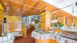 Un espace buffet proposant une variété de plats, un coin salon avec des tables et des chaises, et un mur décoratif orné d’un logo.