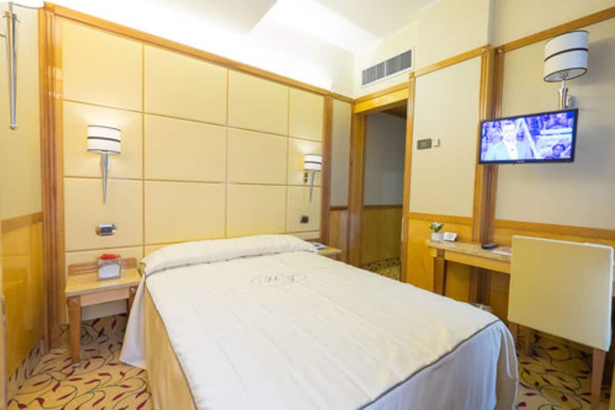 Une chambre d’hôtel comprenant un lit, une table de chevet, une lampe, une télévision et une porte donnant sur une autre pièce.