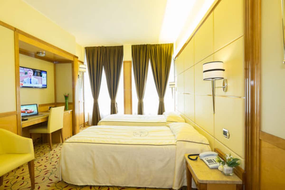 Une chambre d’hôtel avec deux lits, un bureau avec un ordinateur, une chaise, un téléphone et une télévision.