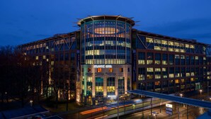 A modern hotel with a circular central atrium, multiple floors, and a prominent entrance. - ATLANTIC Hotel Airport (Bremen)