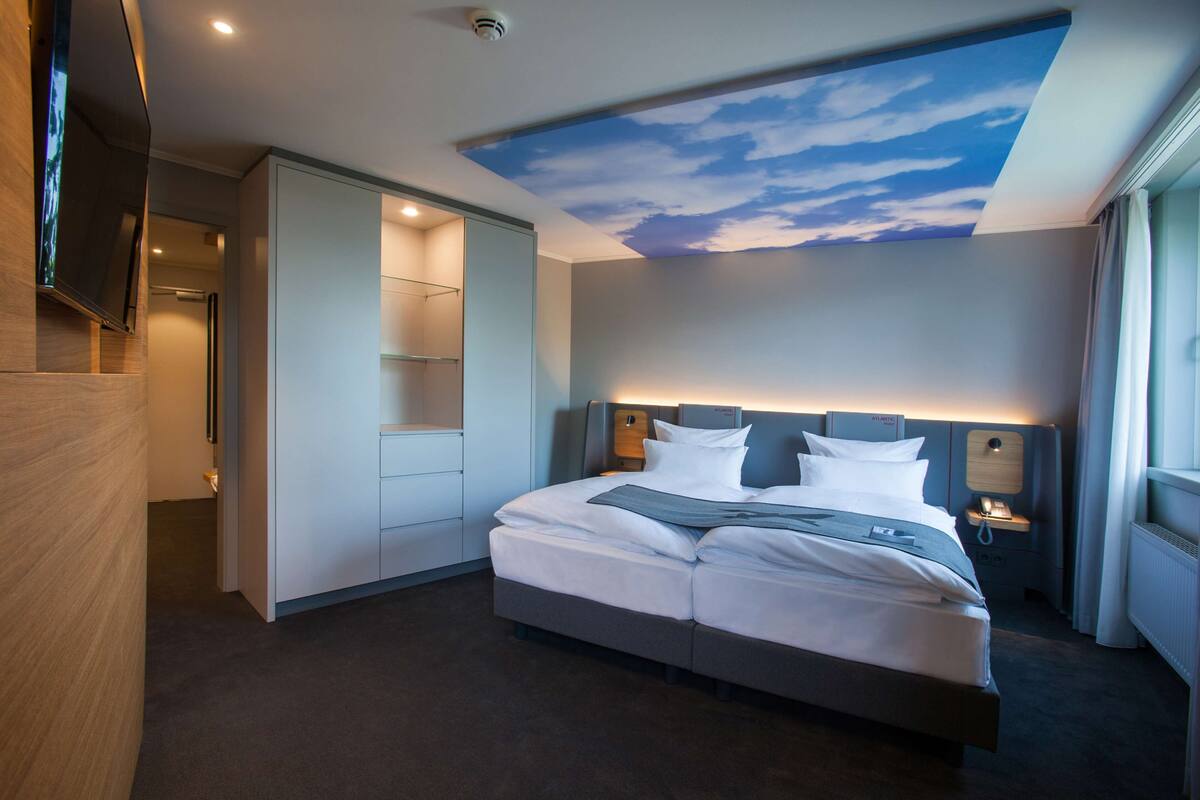 Habitación de hotel con cama, televisor, mesita de noche y un techo decorado con un diseño celeste.