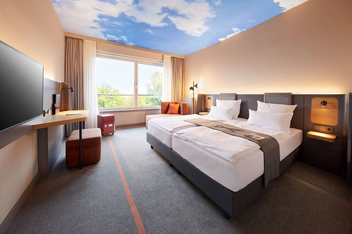 Habitación de hotel con una cama grande, un escritorio, un televisor y una ventana con cortinas.