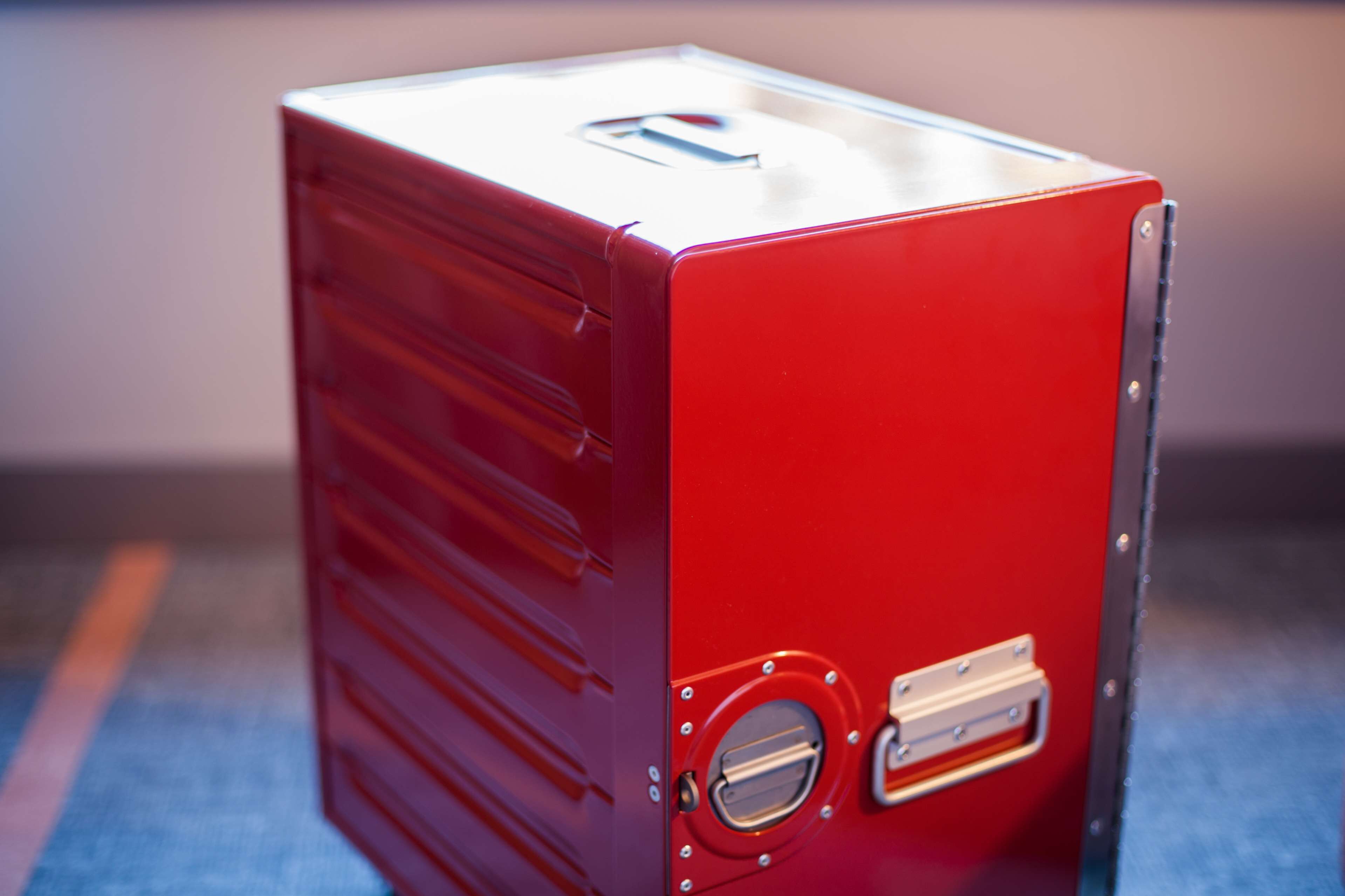 A red metal box with a circular handle and a slot on the side.