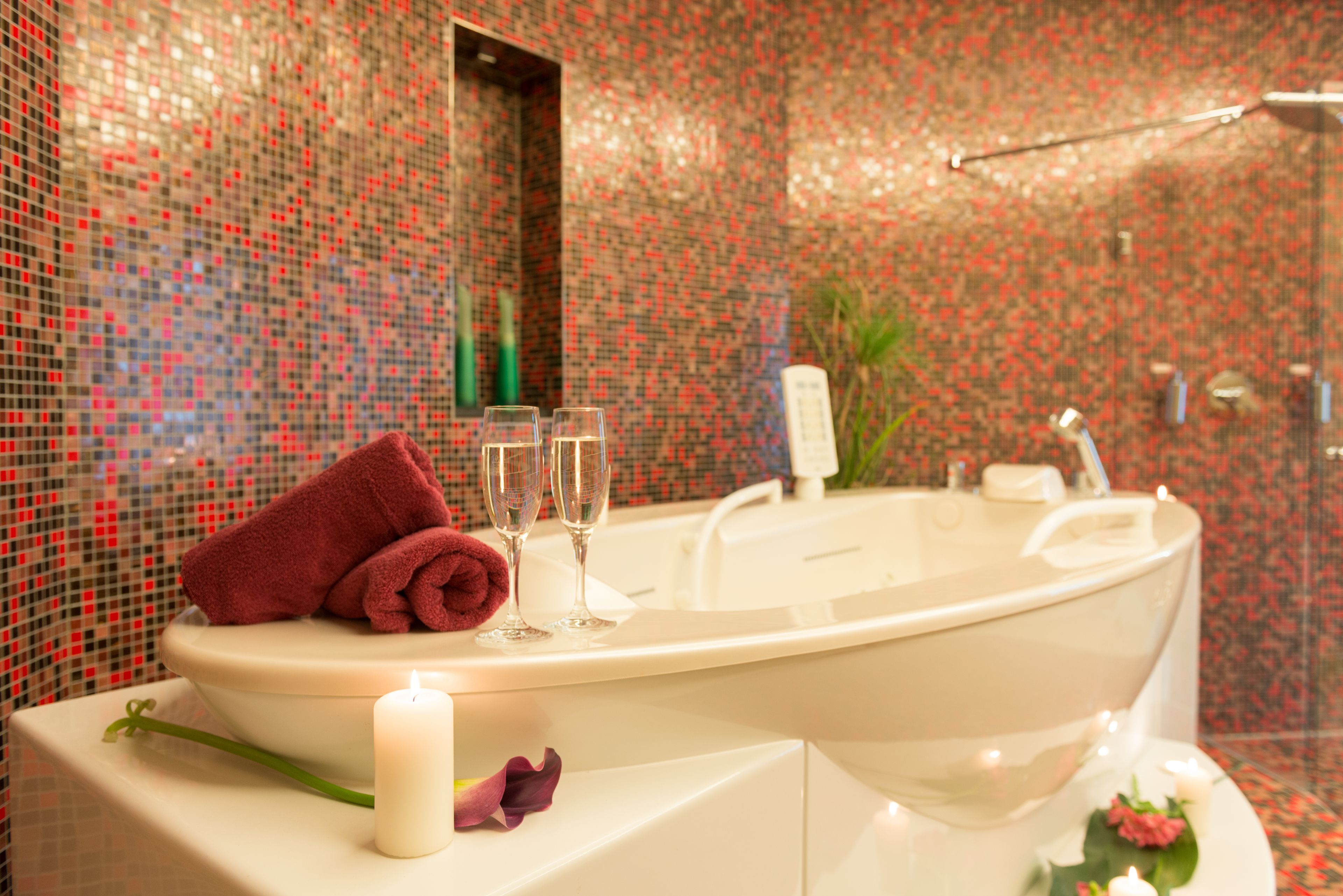 A bathroom with a bathtub, a mirror, a sink, and a decorative arrangement including a towel, two glasses, and a candle.