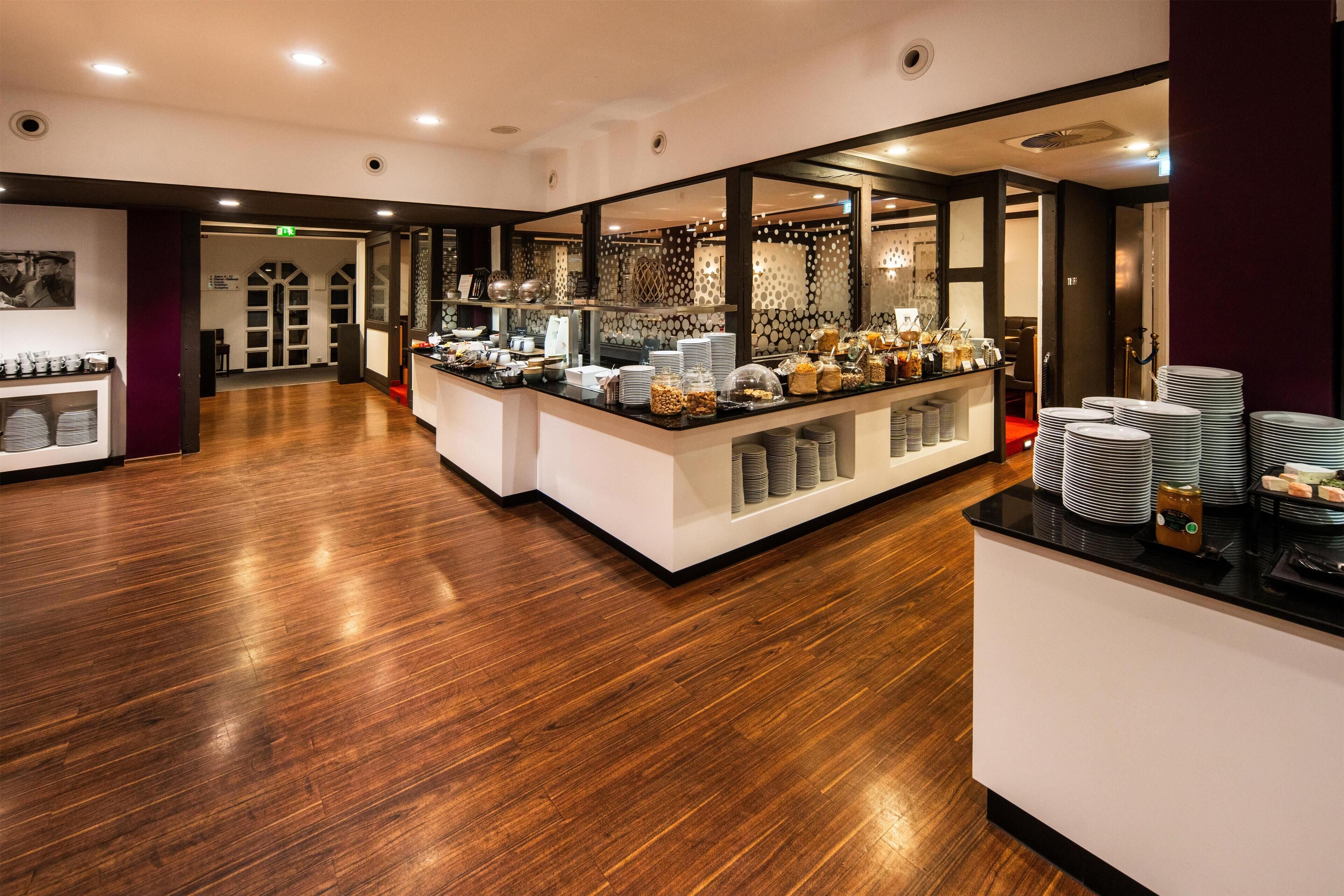 A modern hotel lobby with a reception desk, a buffet area with various food items, and a wooden floor.