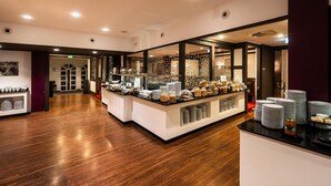 A modern hotel lobby with a reception desk, a buffet area with various food items, and a wooden floor.