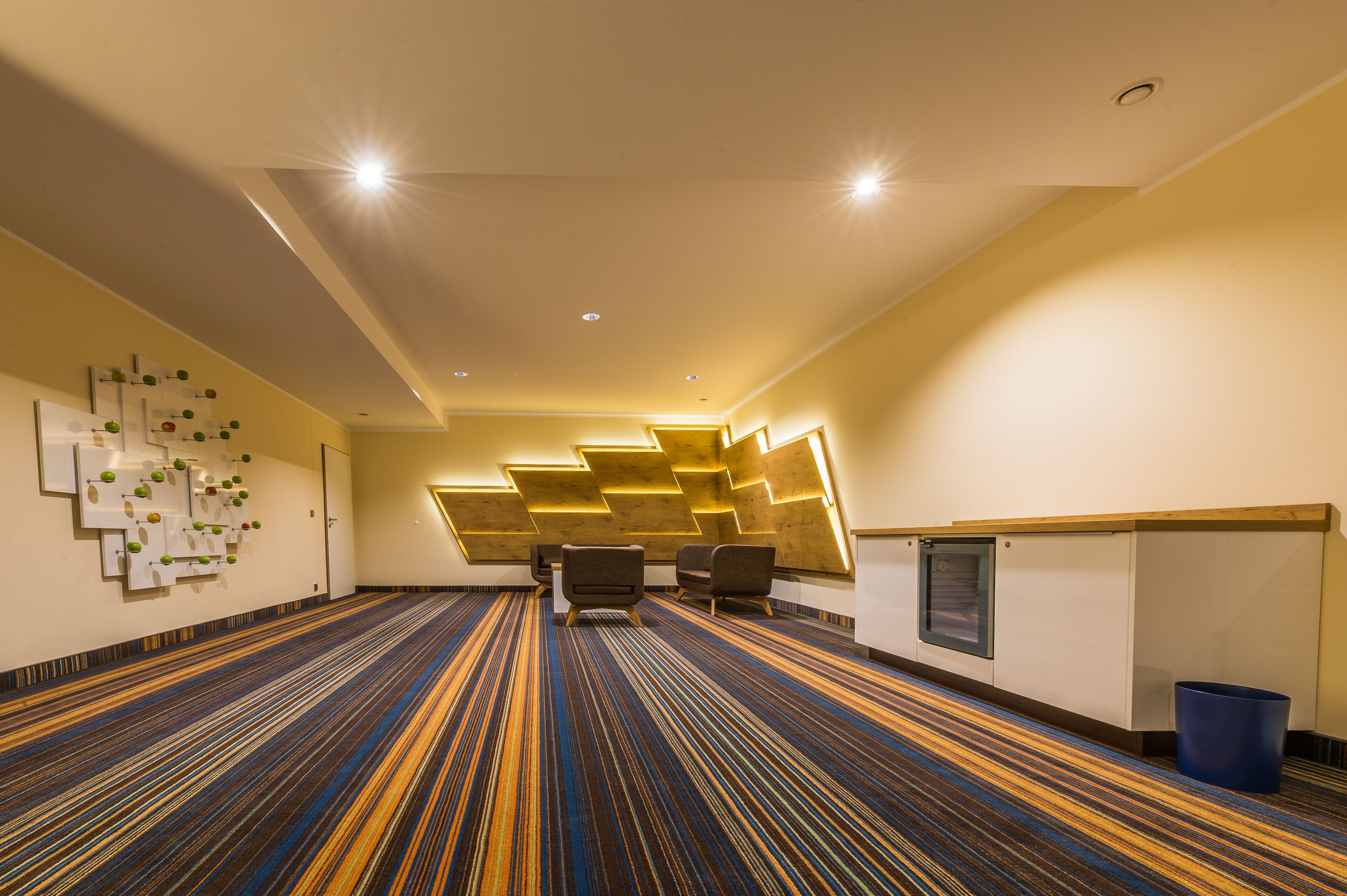 A hotel lobby with a patterned carpet, seating area, and modern lighting fixtures.
