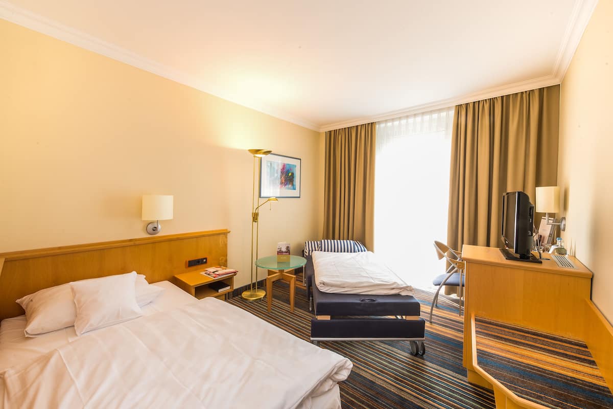 A hotel room with two beds, a desk, a chair, a TV, and a lamp.