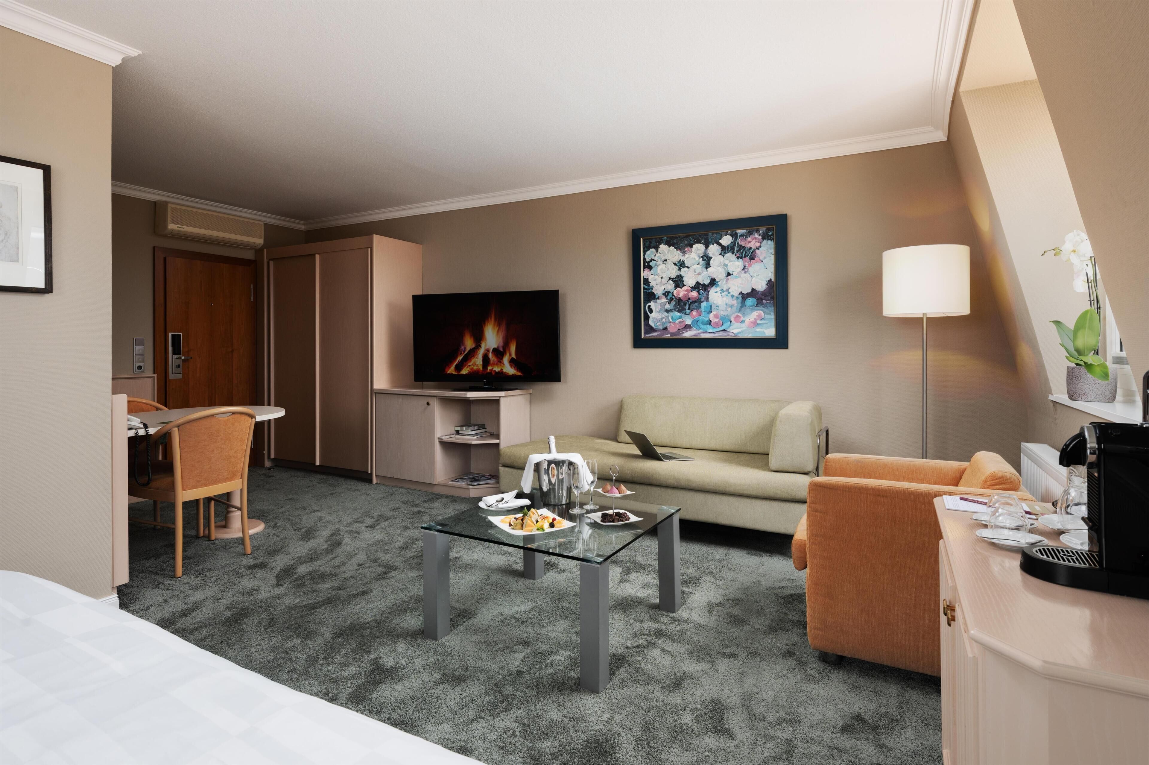 A hotel room with a glass coffee table, a sofa, a TV, and a painting on the wall.