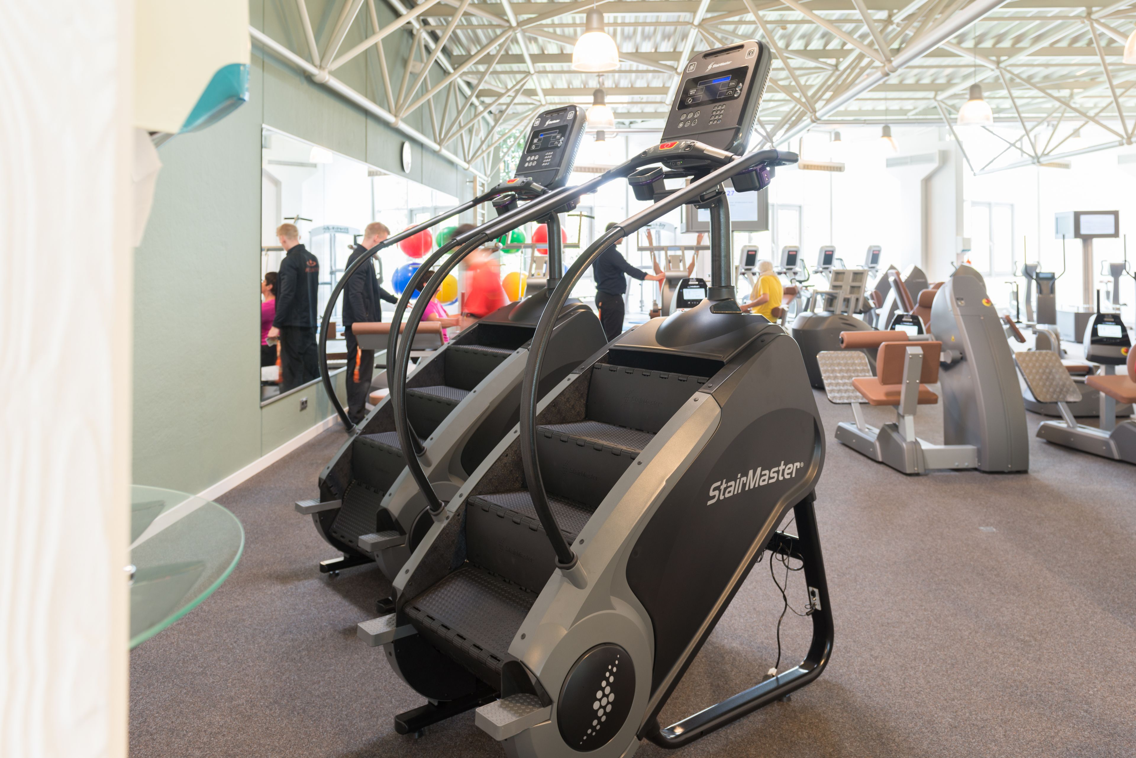 A StairMaster elliptical machine in a gym with other fitness equipment and a glass wall.