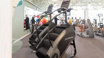 A StairMaster elliptical machine in a gym with other fitness equipment and a glass wall.