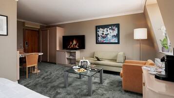 A hotel room with a sofa, armchair, coffee table, TV, and a painting on the wall.