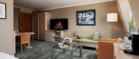 Habitación de hotel con sofá, sillón, mesa de centro, televisor y un cuadro en la pared.