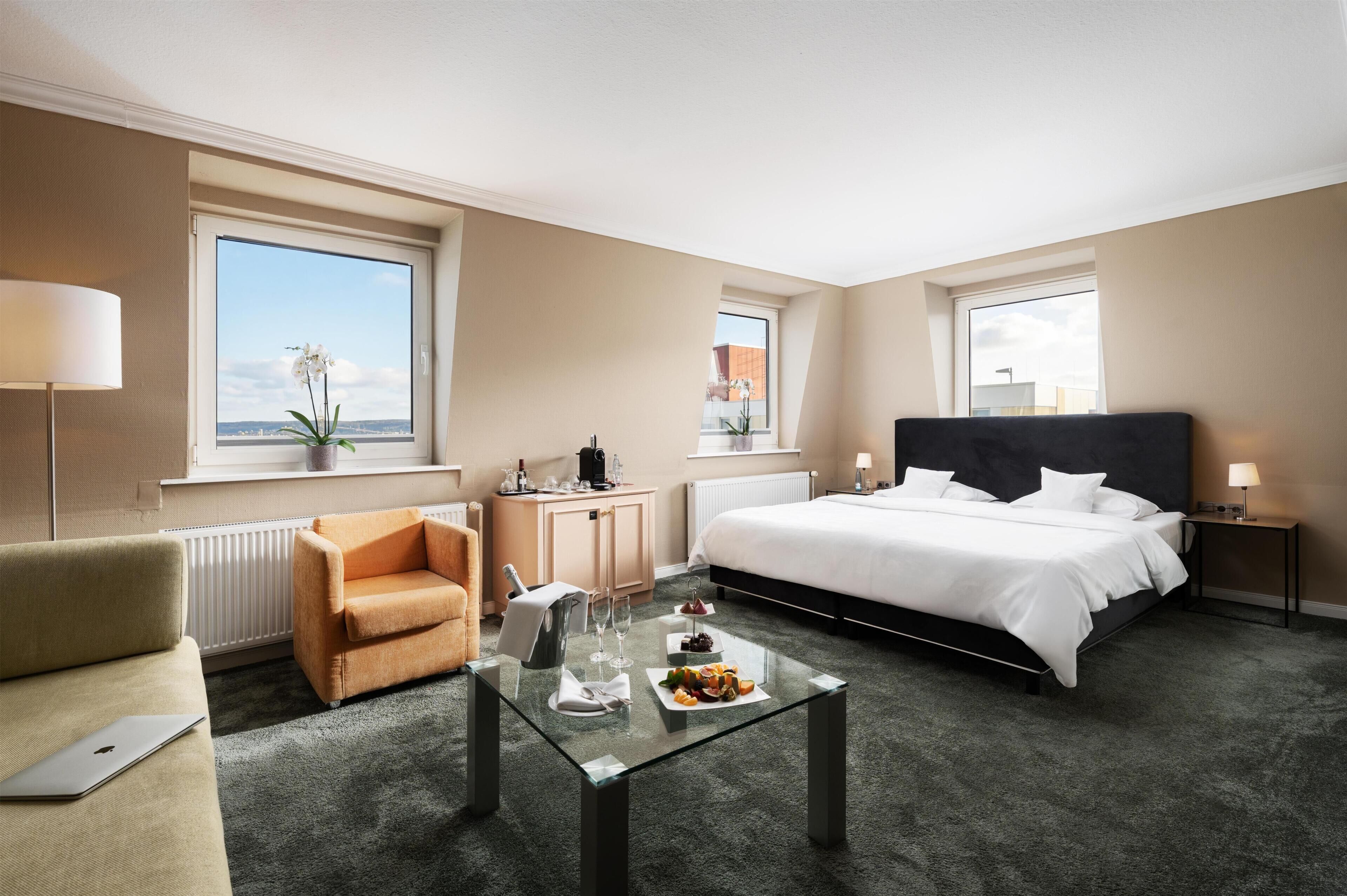 Een hotelkamer met een bed, een bank, een eettafel met eten, een bureau en een raam met uitzicht.