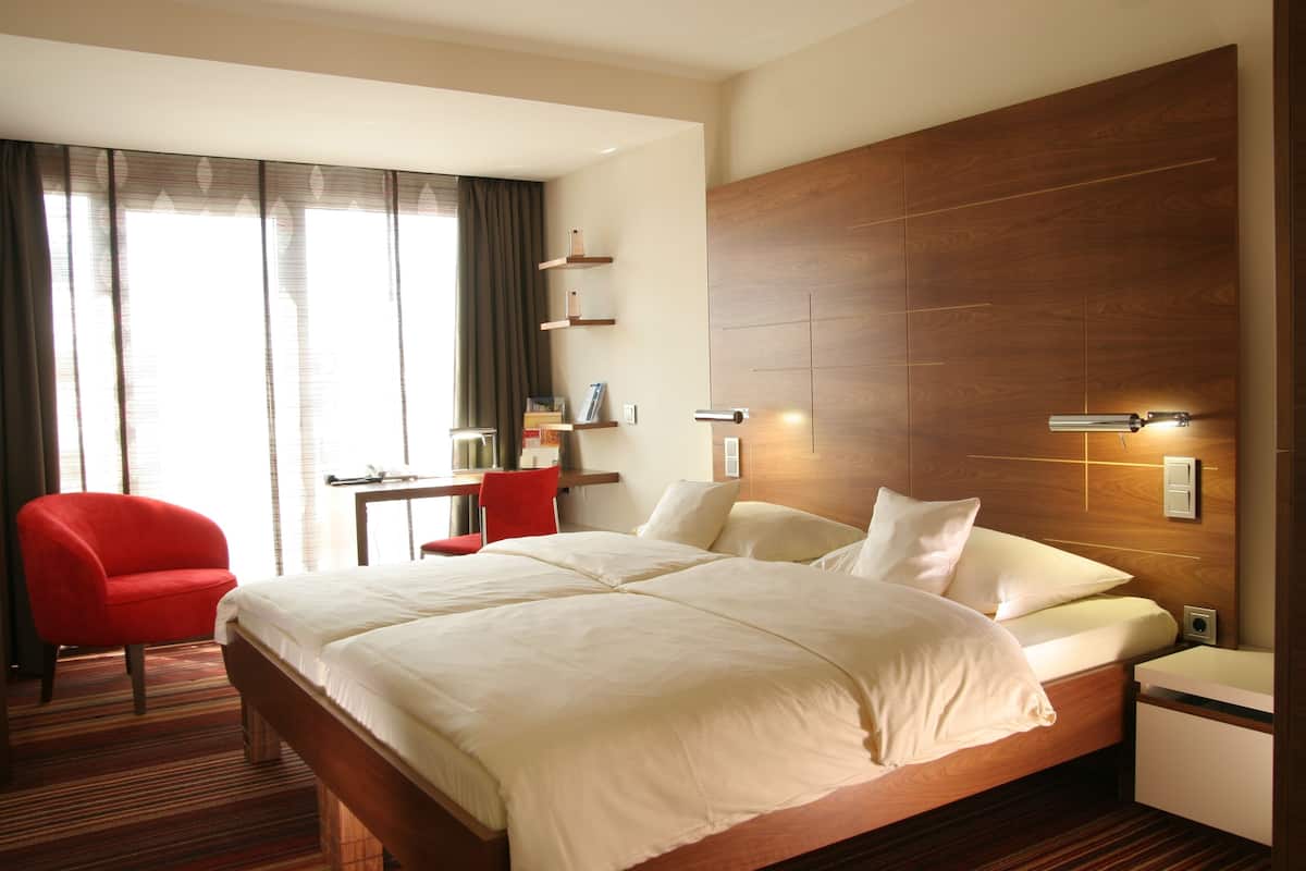 A hotel room with a large bed, a desk, a chair, and a wooden headboard.